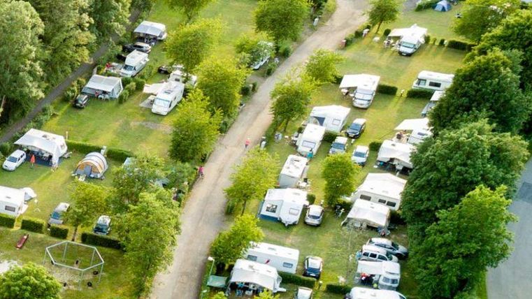 Ein Campingplatz mit vielen Wohnwagen und Bäumen. Es gibt einen klaren Weg zwischen den Stellplätzen.