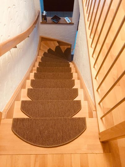 Un escalier lumineux avec une rambarde en bois et un tapis. En haut de l'escalier, il y a une table avec plusieurs objets.
