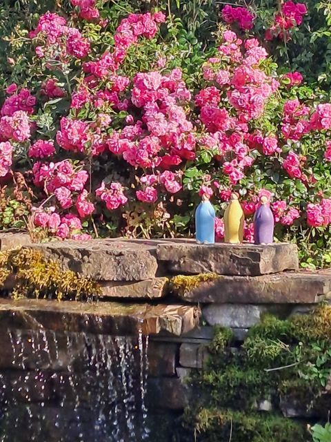 A beautiful stone wall with flowing water and colorful bottles. In the background, pink roses are blooming.