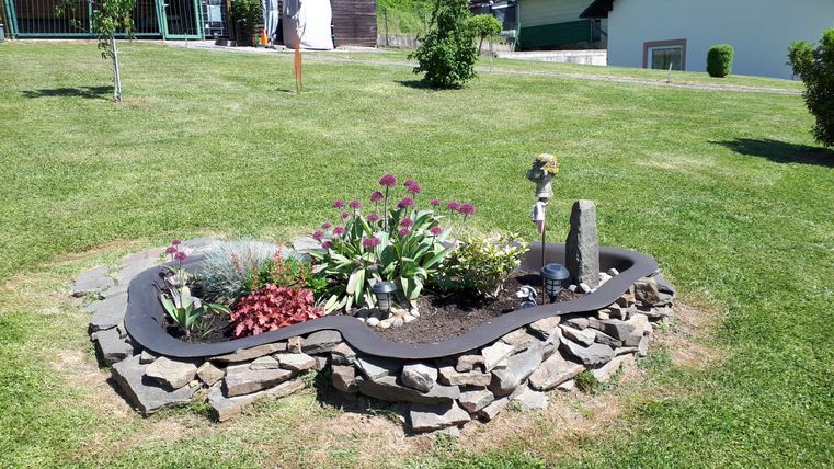 Ein schöner Garten mit bunten Blumen und einem dekorativen Steingarten. Die Anlage hat eine geschwungene Form und ist von grünem Rasen umgeben.