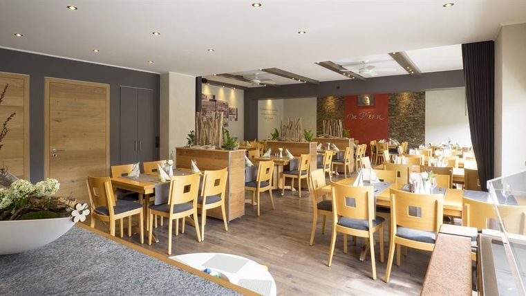 Ein modernes Restaurant mit Tischen und Stühlen aus Holz. Das Raumdesign ist hell und einladend, mit dekorativen Elementen an den Wänden.