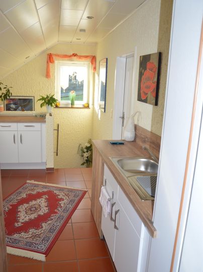 Eine gemütliche Küchenecke mit einem kleinen Waschbecken und einem Teppich. Helle Wände und Pflanzen sorgen für eine freundliche Atmosphäre.