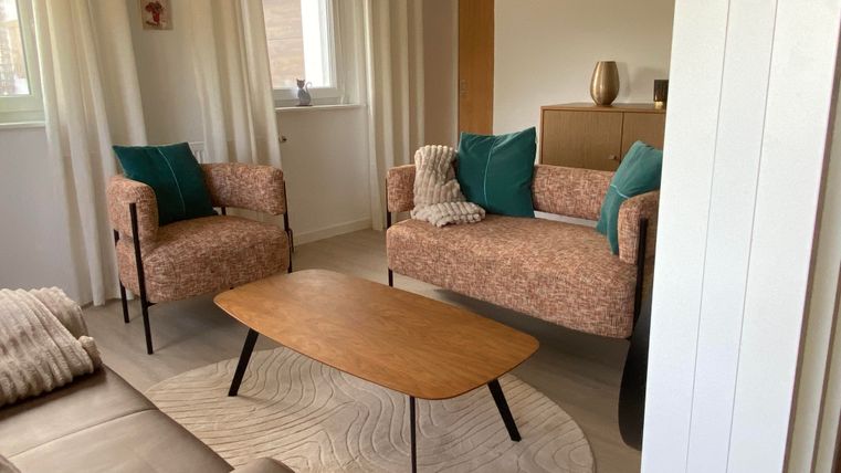 Een modern woonkamer met twee stijlvolle fauteuils en een bank. De houten tafel staat op een rond tapijt en de muren zijn licht geverfd.