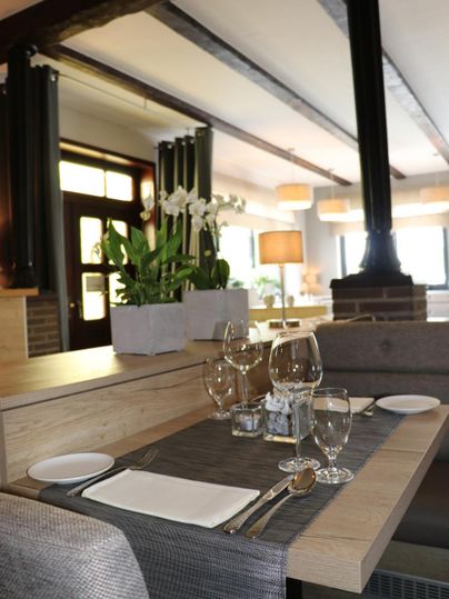 Ein eleganter Restauranttisch mit feiner Tischdeckung und Geschirr. Im Hintergrund sind dekorative Pflanzen und sanfte Beleuchtung sichtbar.