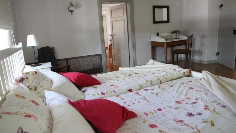 Ein gemütliches Schlafzimmer mit einem großen Bett und bunten Kissen. Im Hintergrund gibt es einen Tisch und eine Lampe.