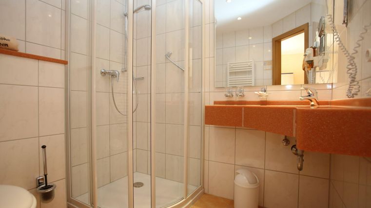 Ein modernes Badezimmer mit einer Duschkabine und hellen Fliesen. Der Waschbereich verfügt über einen großen Spiegel und eine praktische Ablage.