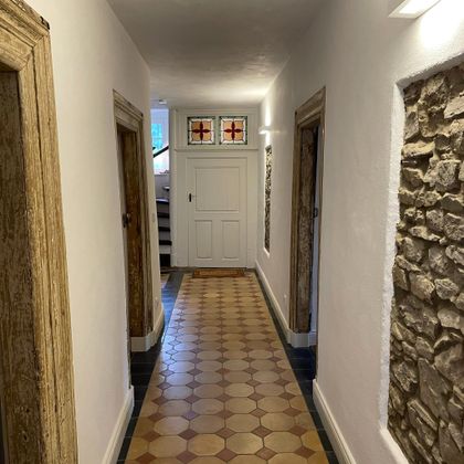 A bright hallway with a colorful tiled floor and natural stone walls. Doors are located on both sides, leading to different rooms.