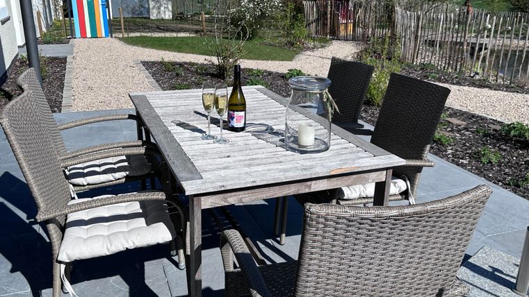 A furnished outdoor area with a table and chairs. On the table are two champagne glasses and a bottle.