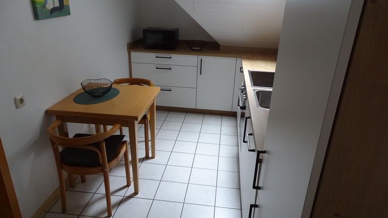 Eine kleine, moderne Küche mit einem Tisch und Stühlen. Die Wände sind hell, und es gibt eine Mikrowelle sowie Küchenmöbel.