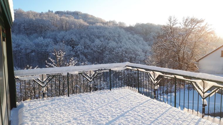 Eine verschneite Terrasse mit Blick auf einen winterlichen Wald. Die Sonne scheint und taucht die Szene in warmes Licht.