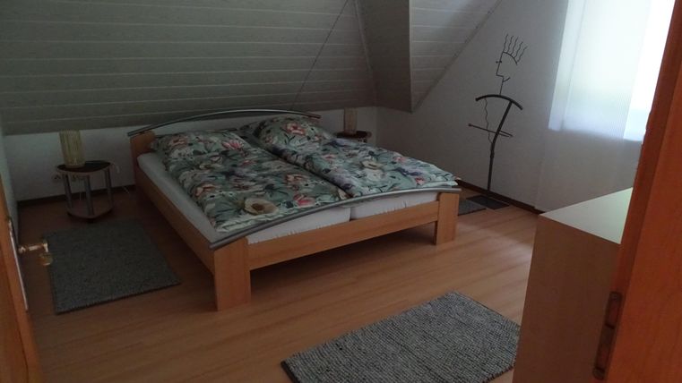 Ein gemütliches Schlafzimmer mit einem Doppelbett und floralem Bettzeug. Der Raum hat einen schrägen Dachstuhl und einen modernen Dekorationsgegenstand in der Ecke.