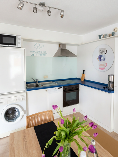 Een moderne keuken met witte kasten en een blauwe werkblad. Op de tafel staat een boeket mooie tulpen in een vaas.