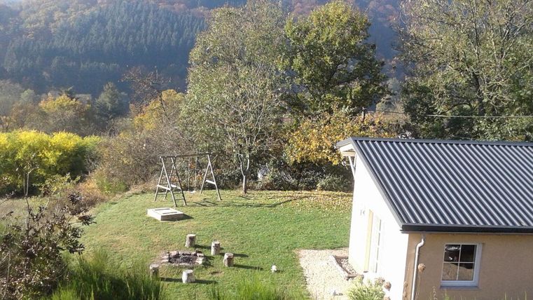 Ein gemütliches Haus umgeben von Bäumen und einer grünen Wiese. Im Hintergrund sieht man sanfte Hügel und bunte Herbstblätter.