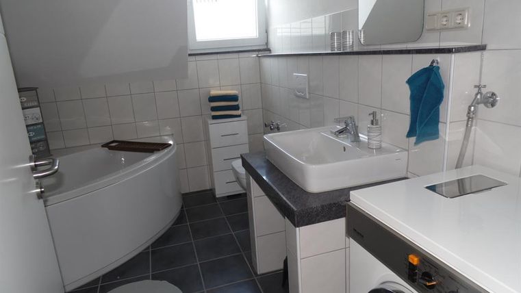 Ein modernes Badezimmer mit einer Badewanne und einer Waschmaschine. Es gibt ein Waschbecken und helle Fliesen, die den Raum sauber und einladend wirken lassen.