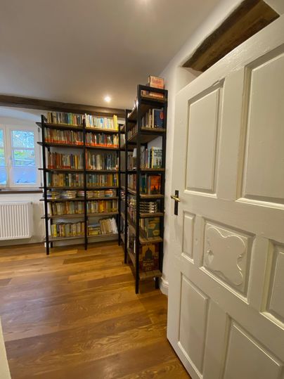 A cozy room with bookshelves on the walls and a white door. The floor is made of wood and the light is bright.