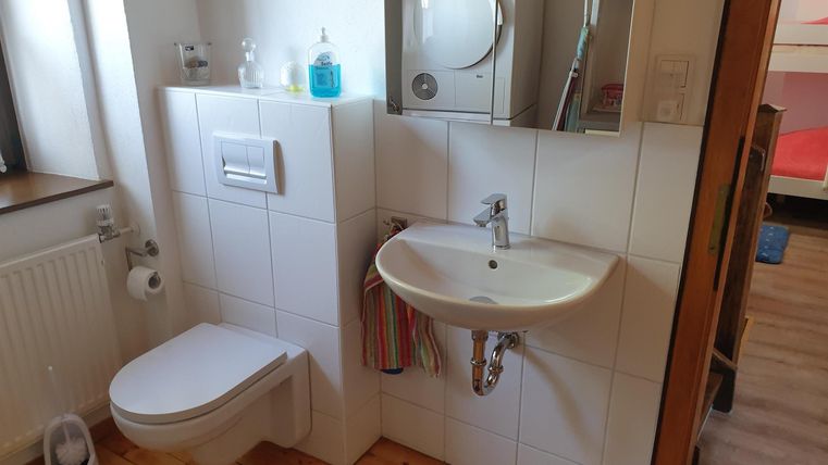Ein modernes Badezimmer mit einer Toilette und einem Waschbecken. Die Wände sind hell gefliest und es gibt einen Spiegel sowie eine Waschmaschine im Hintergrund.
