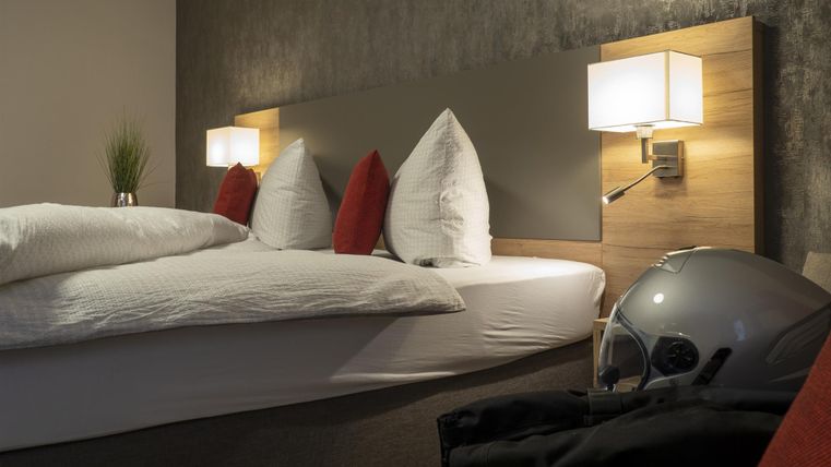 Ein modernes Schlafzimmer mit einem bequemen Bett und gemütlicher Beleuchtung. Ein Motorradhelm liegt neben dem Bett, was auf ein aktives Lifestyle hinweist.
