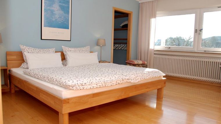 Une chambre lumineuse avec un grand lit et des coussins confortables. Les murs sont peints en bleu et une grande fenêtre apporte beaucoup de lumière naturelle.