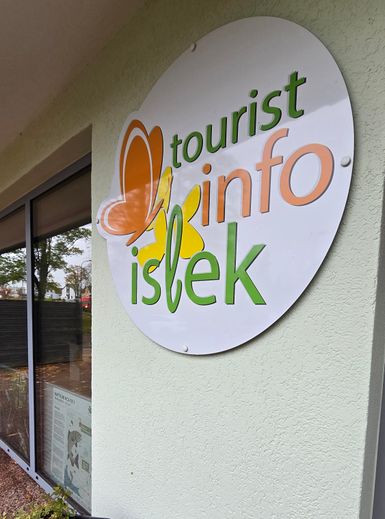 Ein Schild mit der Aufschrift "tourist info islek" und einem Schmetterling. Die Farben sind orange, grün und gelb, und es befindet sich an einer Wand.