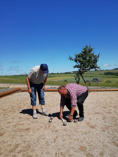 Zwei Männer spielen im Freien mit einem Spiel. Die Szene zeigt eine grüne Landschaft unter klarem blauen Himmel.
