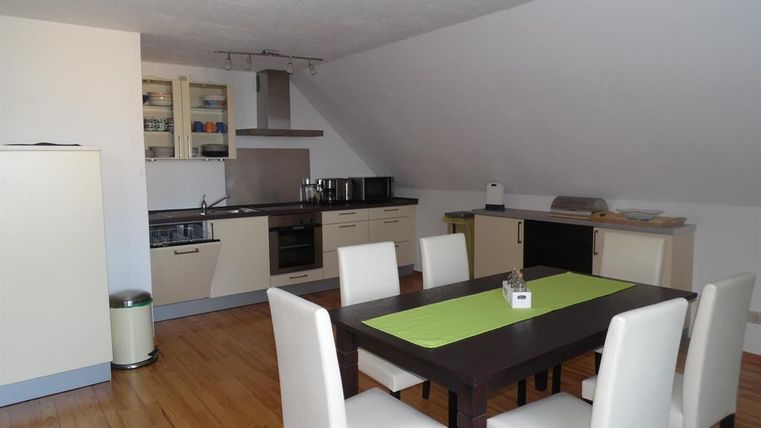 Moderne Küche mit eleganten Möbeln und einem großen Esstisch. Der Raum ist hell und freundlich mit Holzfußboden und hochwertigen Geräten.