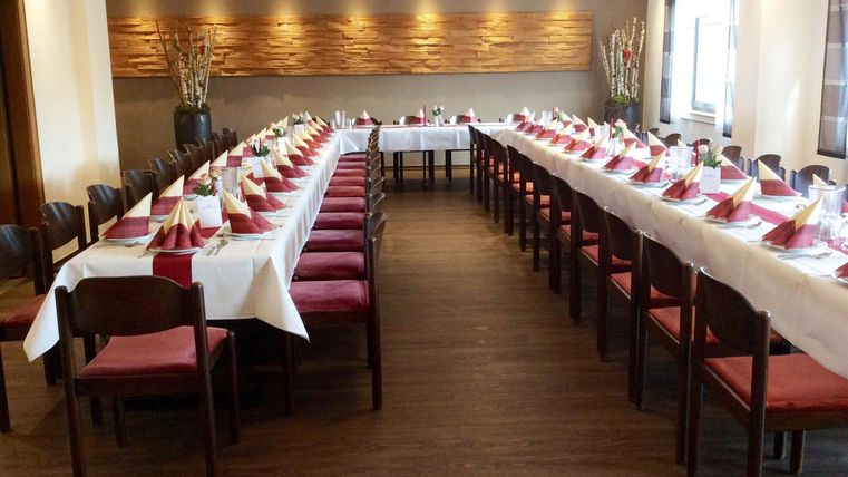Ein eleganter Veranstaltungsraum mit langen Tischen, die festlich eingedeckt sind. Rote Servietten und stilvolle Dekoration schaffen eine einladende Atmosphäre.
