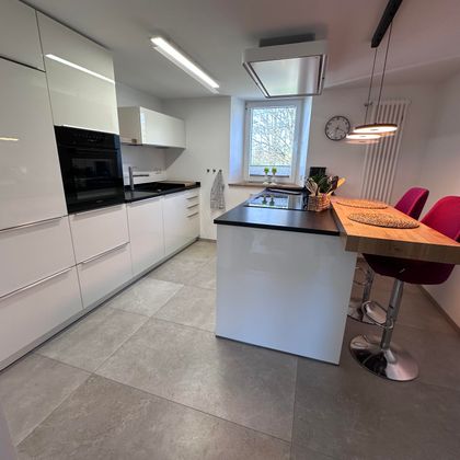 Modern kitchen with white cabinets and a mix of dark and light surfaces. A breakfast bar with red stools complements the elegant design.