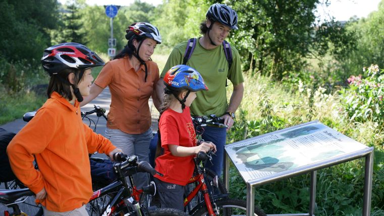 Familie mit Fahrrädern liest Infotafel über Biber auf dem Eifel-Ardennen-Radweg.