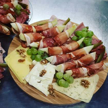 An attractively arranged plate with various types of sausage and cheese, grapes, and nuts. The dishes are artfully arranged on a round wooden board.