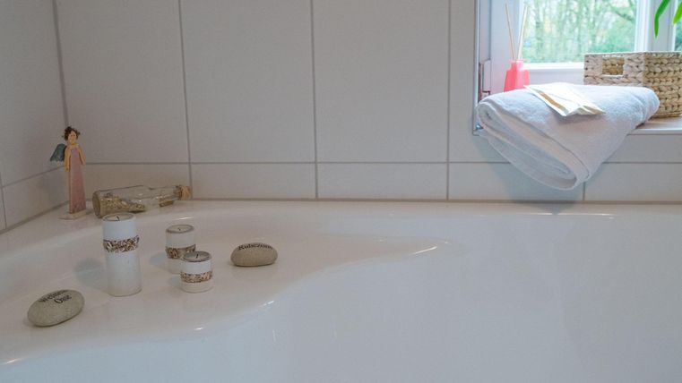 Ein Badezimmer mit einer weißen Badewanne und einigen dekorativen Elementen. Auf dem Fensterbrett liegen Handtücher und kleine Accessoires.