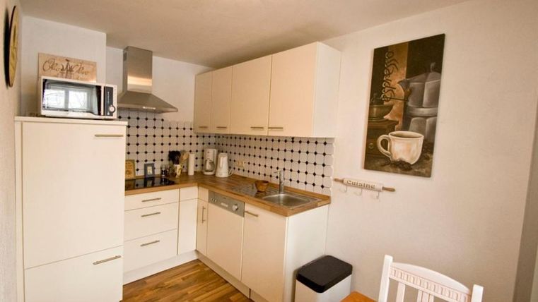 Eine moderne Küche mit hellen Schränken und Holzfußboden. Die Ausstattung umfasst einen Herd, eine Spüle und einen Esstisch.