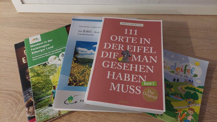 A collection of travel guides about the Eifel, lying on a table. The main title emphasizes: "111 Places in the Eifel You Must See."