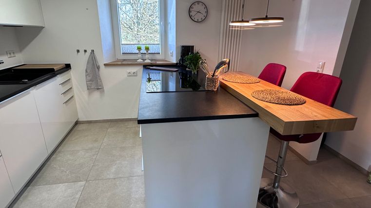 A modern kitchen with a cooking island and two red bar stools. Light streams through the window, creating an inviting atmosphere.