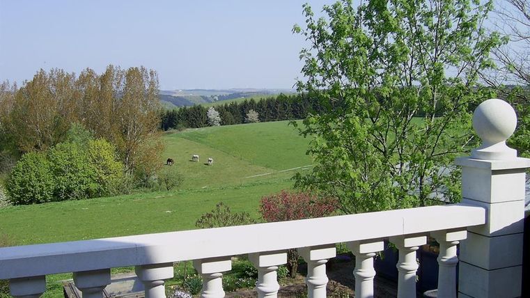 Un paysage calme avec une vaste prairie et quelques vaches. Au premier plan, on peut voir un balcon avec une balustrade.