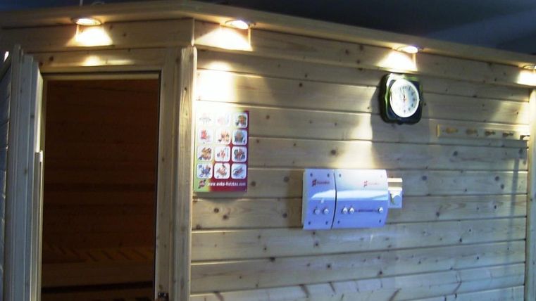 Un intérieur avec un sauna en bois, accentué par un éclairage chaud. Sur le mur, une horloge et des documents d'information sont accrochés.