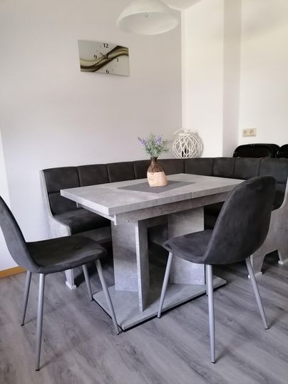 Une salle à manger moderne avec une table grise et un banc. Sur la table, il y a un petit vase de fleurs, et il y a deux chaises élégantes.