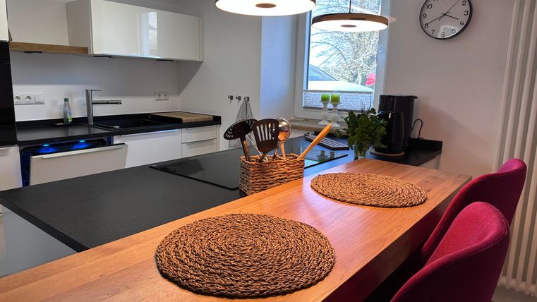 A modern kitchen with a wooden countertop and elegant furniture. There are placemats on the table, and there is plenty of daylight from a window.