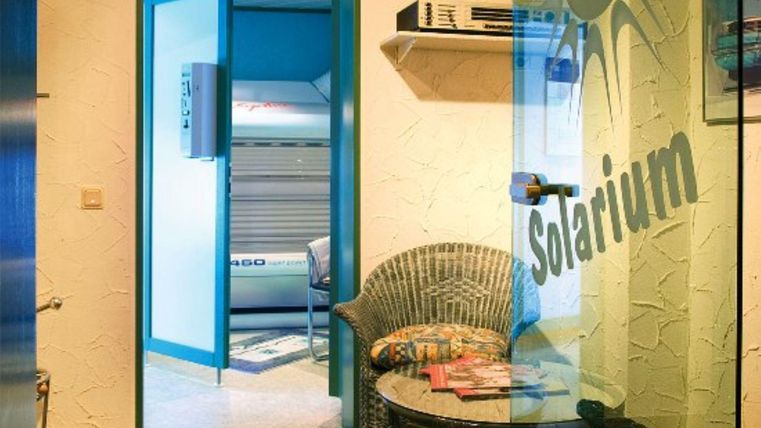 Ein heller Raum mit Zugang zu einem Solarium. Es gibt einen Stuhl und Zeitschriften auf einem Tisch.