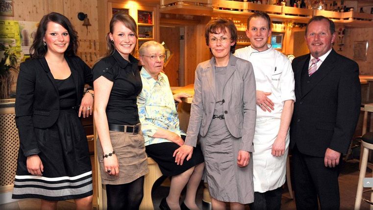 Eine Gruppe von sechs Personen steht in einem Restaurant. Sie lächeln freundlich und posieren gemeinsam für das Foto.