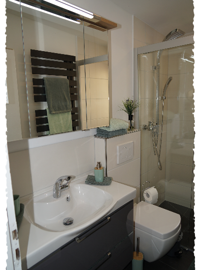 Ein modernes Badezimmer mit Waschbecken, Dusche und hellen Fliesen. Die Möbel sind in neutralen Farben gehalten und es gibt dekorative Elemente wie Handtücher und Pflanzen.