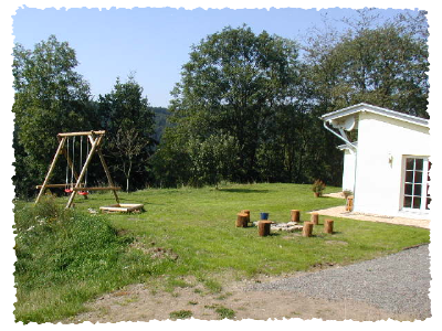 Ein großzügiger Garten mit einer Schaukel und einem Feuerplatz aus Holz. Im Hintergrund sind grüne Bäume und ein helles Haus zu sehen.