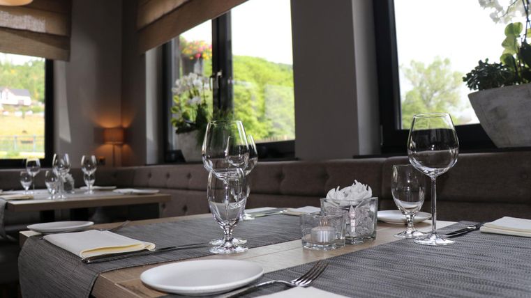 Ein elegantes Restaurant mit schön eingedeckten Tischen. Die Fenster bieten einen Blick auf die grüne Umgebung.