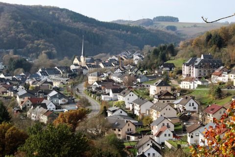 Ein malerisches Dorf mit hübschen Häusern und einer Kirche. Die umliegende Landschaft ist grün und sanft geschwungen.