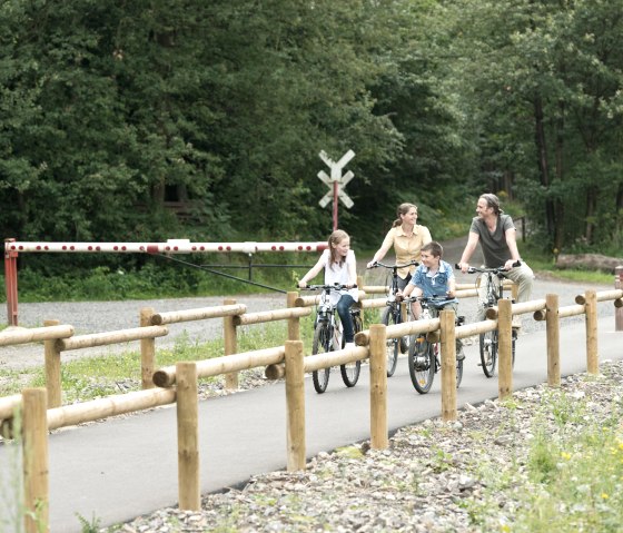 Familie auf Fahrrädern auf der Vennbahn bei Raeren, umgeben von Wald und Holzgeländern., © vennbahn.eu