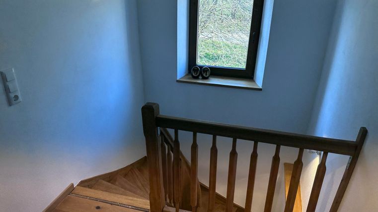 A staircase with a wooden railing and a window that lets light in. The floor is made of wood and the walls are painted light.