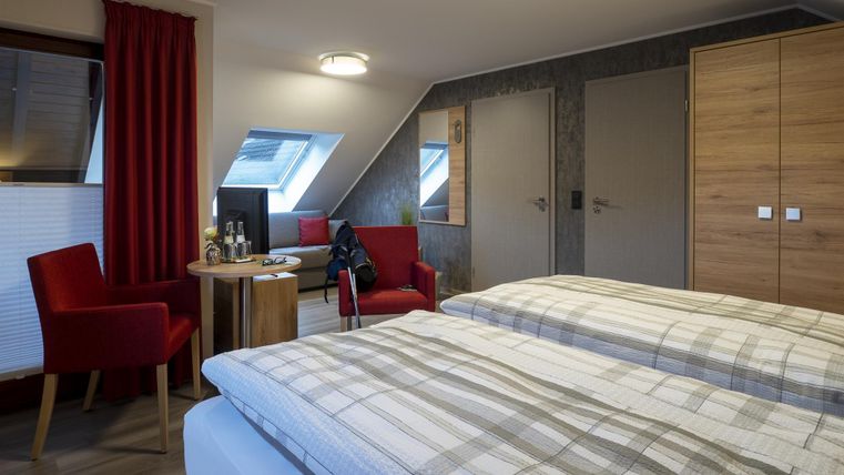 Ein gemütliches Zimmer mit zwei Betten, einem Tisch und einem roten Stuhl. Der Raum hat eine moderne Einrichtung und eine angenehme Atmosphäre.