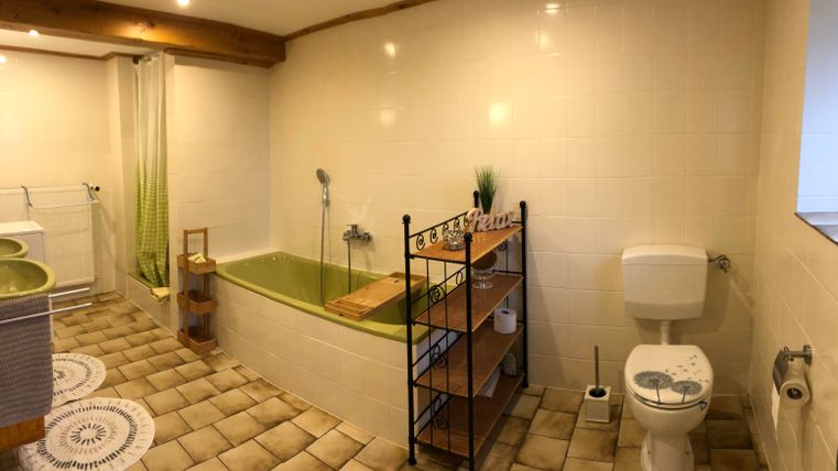 Une salle de bains moderne avec une baignoire, un WC et une étagère. Les murs sont carrelés en clair et le sol a une belle texture de carrelage.