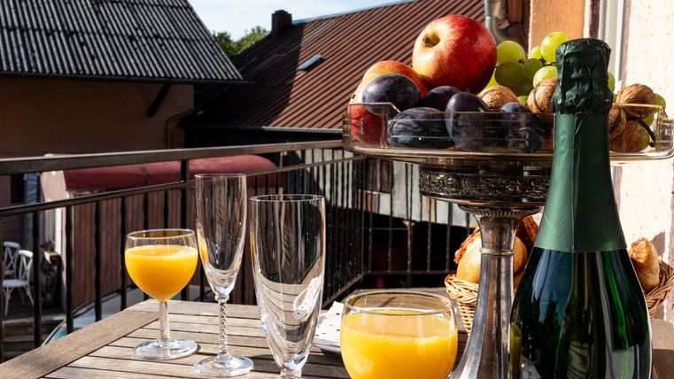 Ein Tisch auf einem Balkon mit Sektflasche, Gläsern und frischem Obst. Die Sonne scheint auf die appetitliche Anordnung.