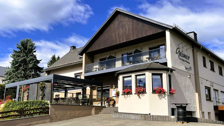 Ein charmantes Haus mit blühenden Balkonpflanzen. Die sonnige Fassade und der einladende Außenbereich schaffen eine freundliche Atmosphäre.