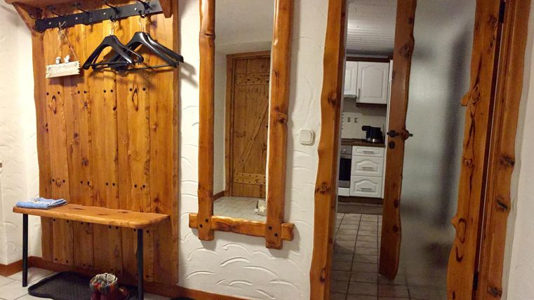 Un couloir élégant avec des murs en bois et un grand miroir. Par une porte, une cuisine est visible.